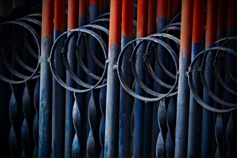 A photograph of a folded metal gate. The folded parts form a repetitive blue and red pattern.